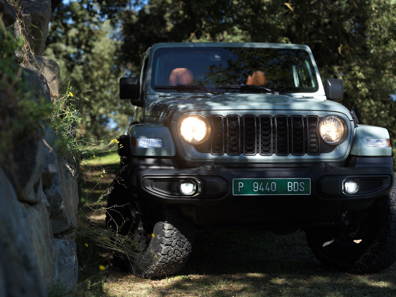 The front of a Jeep Wrangler Rubicon among the trees, headlights on